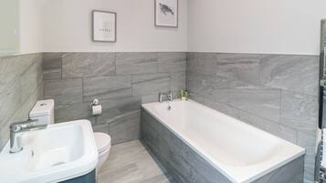 A modern bathroom with a bathtub, a sink, and a toilet. There are two framed pictures on the wall.