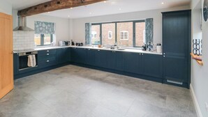 A modern kitchen with dark blue cabinets, a large island, and a wooden beam ceiling. - The Stables (Thirsk)