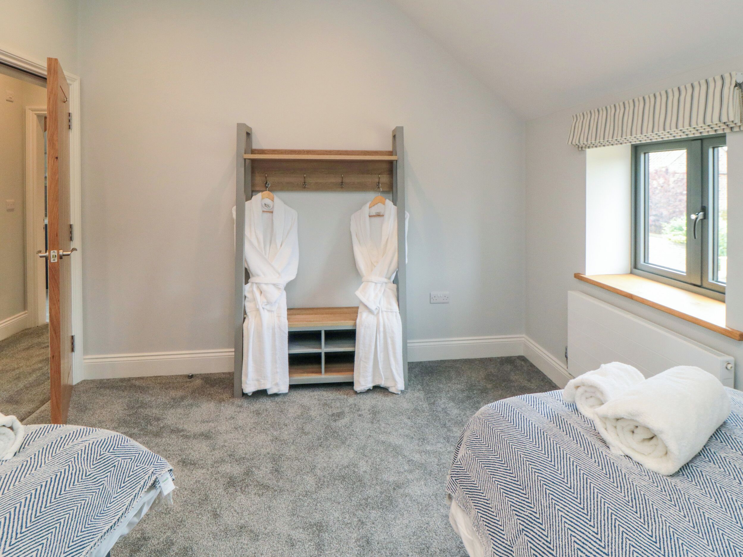 A room with two beds, a wooden bench, and a robe rack with two robes.