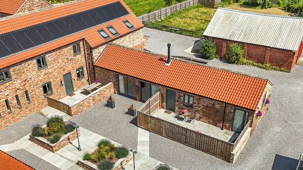 A courtyard with a brick building, a wooden deck, and a small garden area. - The Stables (Thirsk)