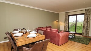Een eethoek met een houten tafel gedekt voor vier personen, een rode bank en uitzicht op een groen veld door een groot raam.