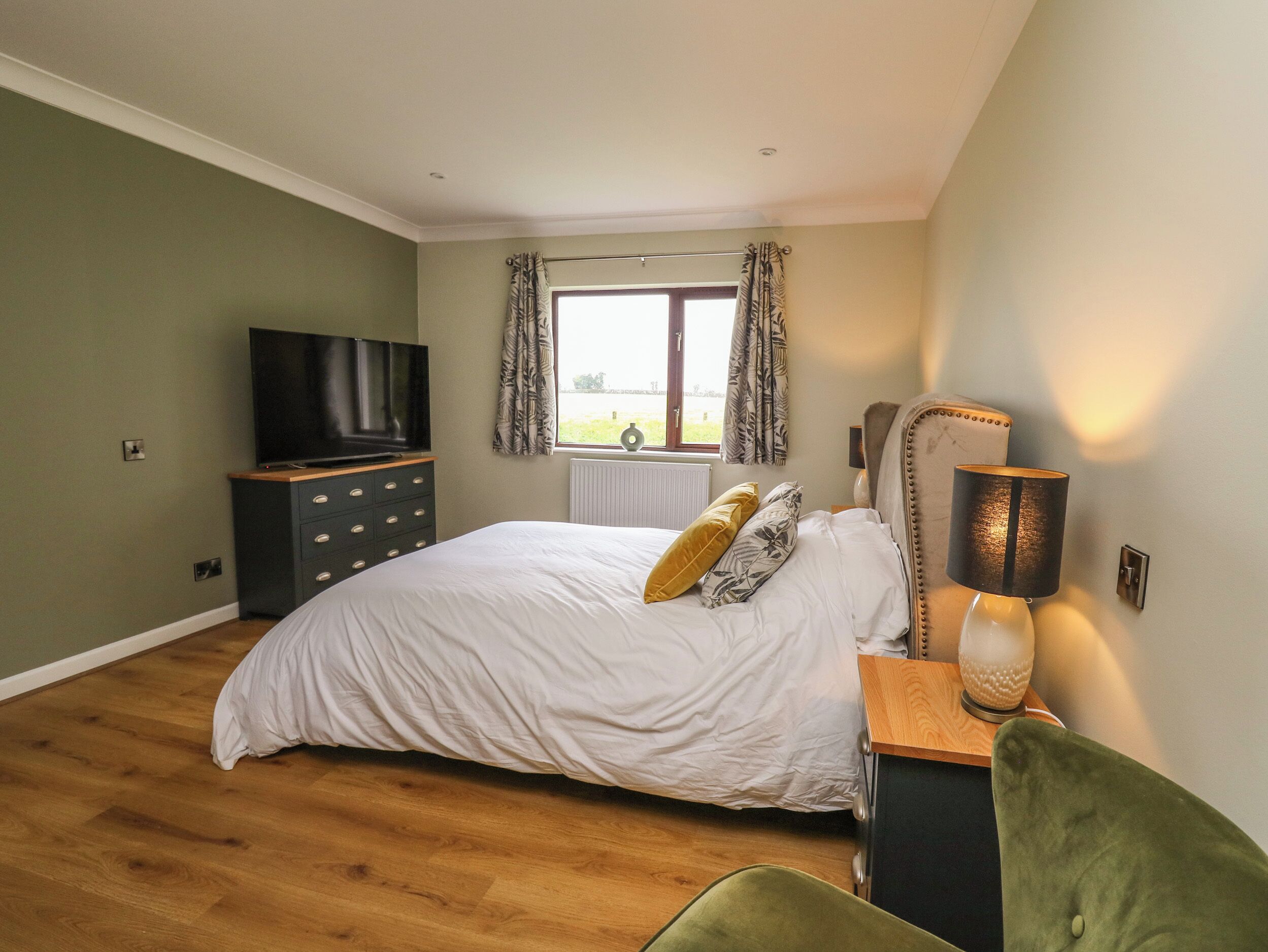 A bedroom with a bed, a television, a window with curtains, and a lamp.