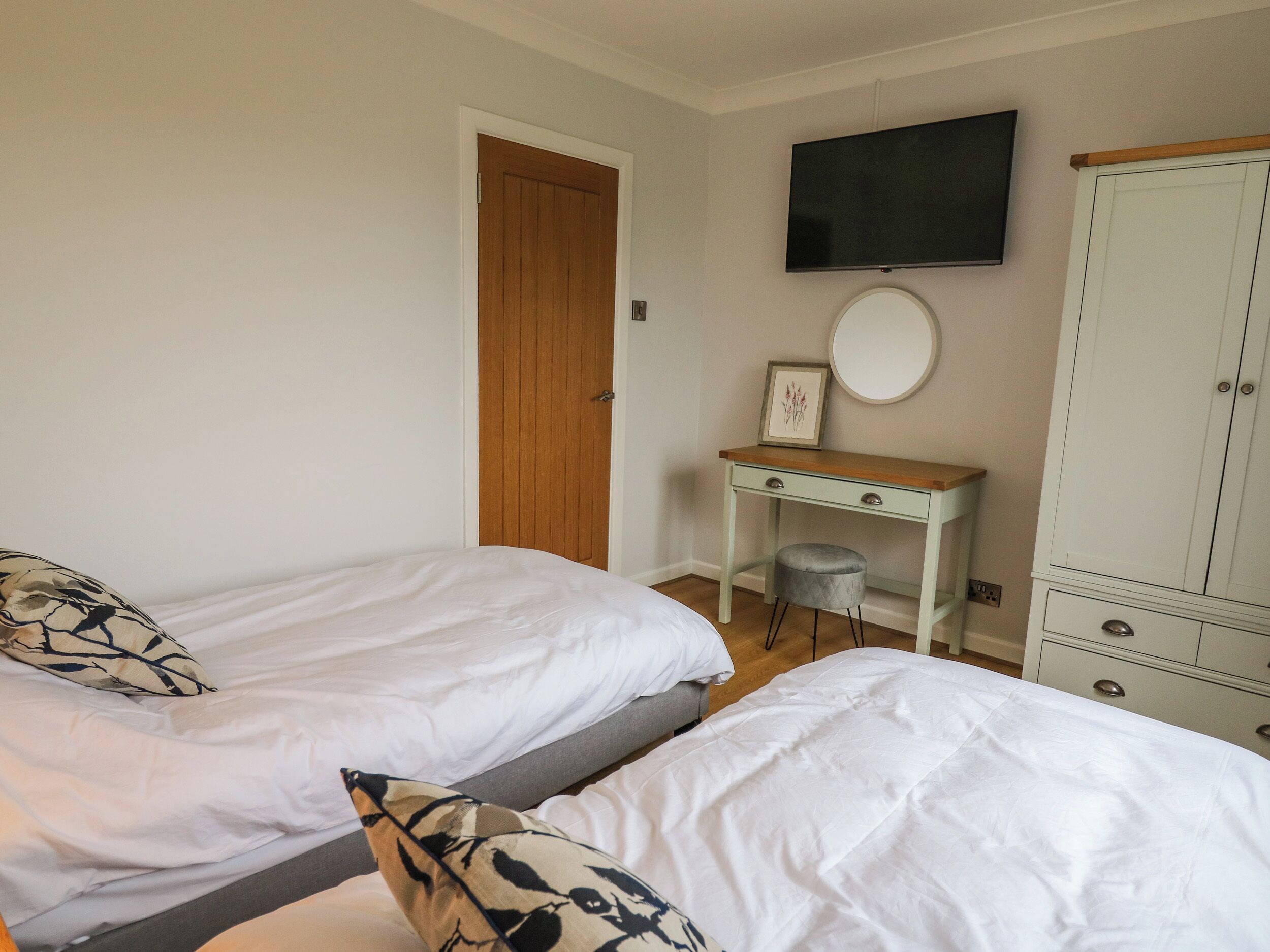 A bedroom with two single beds, a desk with a chair, a wardrobe, and a television on the wall.