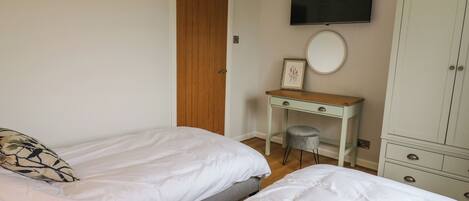 A bedroom with two single beds, a desk with a chair, a wardrobe, and a television on the wall.