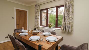 A dining room with a wooden table set for four, a window with curtains, and a door.