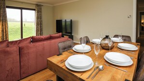Een eetgedeelte met een houten tafel voor vier personen, een bank en een televisie op de achtergrond.