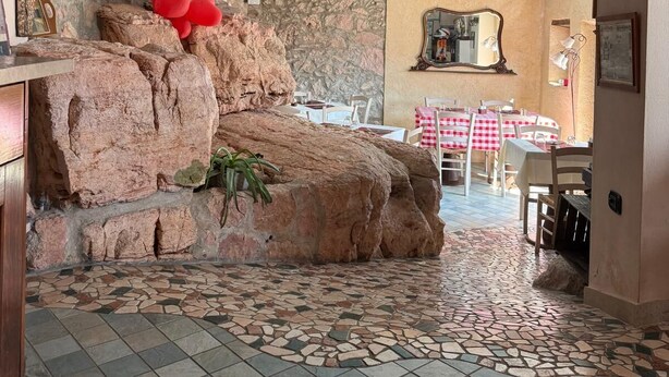Uma área de refeições com parede de pedra, piso de azulejos e balões vermelhos. Há pôsteres de filmes emoldurados na parede.