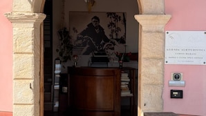 Entrada com arco de pedra que leva a um quarto com escrivaninha, cadeira e placa na parede.