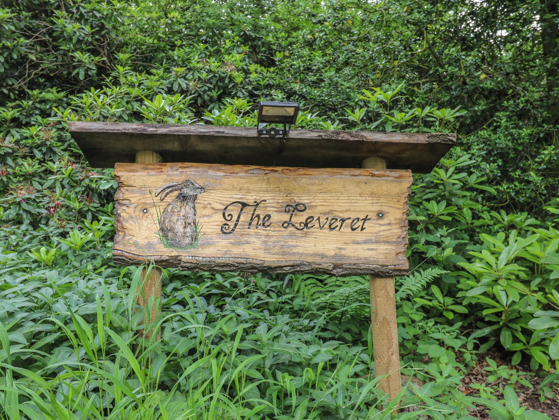 A wooden sign with a rabbit illustration and the text 'The Leveret' in a garden setting.