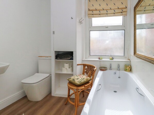 A bathroom with a toilet, a sink, a bathtub, a wicker chair, and a window with a view. - 26 High West (Weymouth)