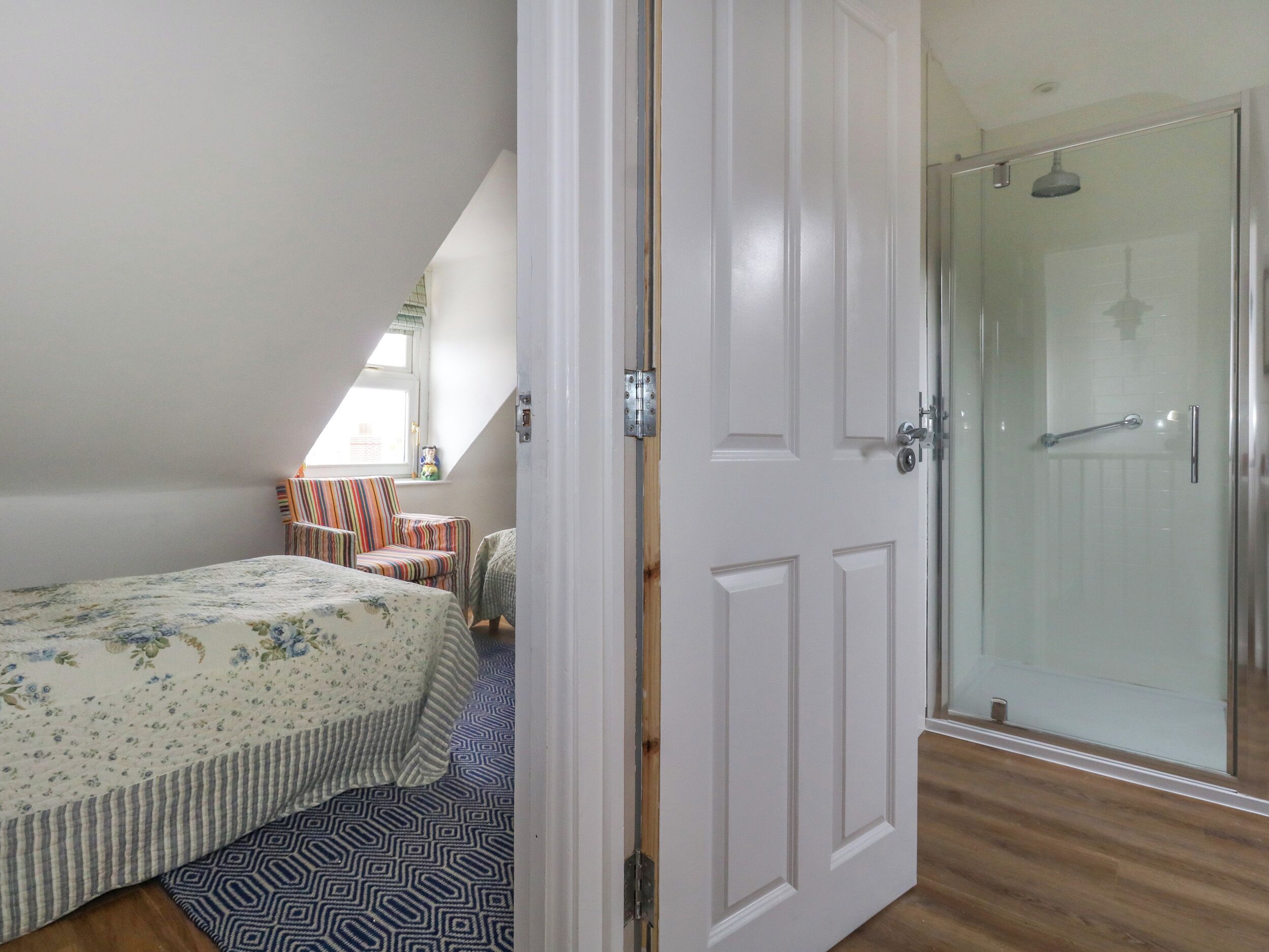 A bedroom with a bed, a striped chair, a small table, and a glass shower door.
