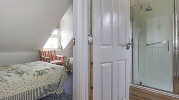 Une chambre à coucher avec un lit, une chaise à rayures, une petite table et une porte de douche en verre.