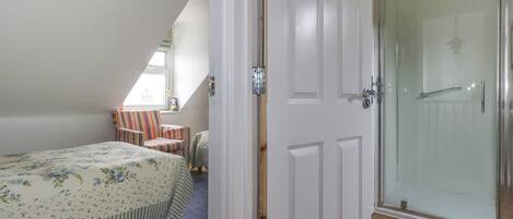 A bedroom with a bed, a striped chair, a small table, and a glass shower door.