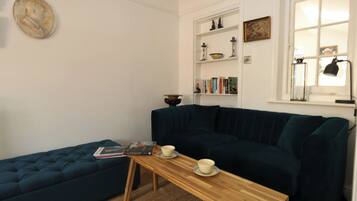 Una sala de estar acogedora con un sofá azul oscuro, una mesa de centro de madera con una revista y una taza, y una estantería con diversos objetos.