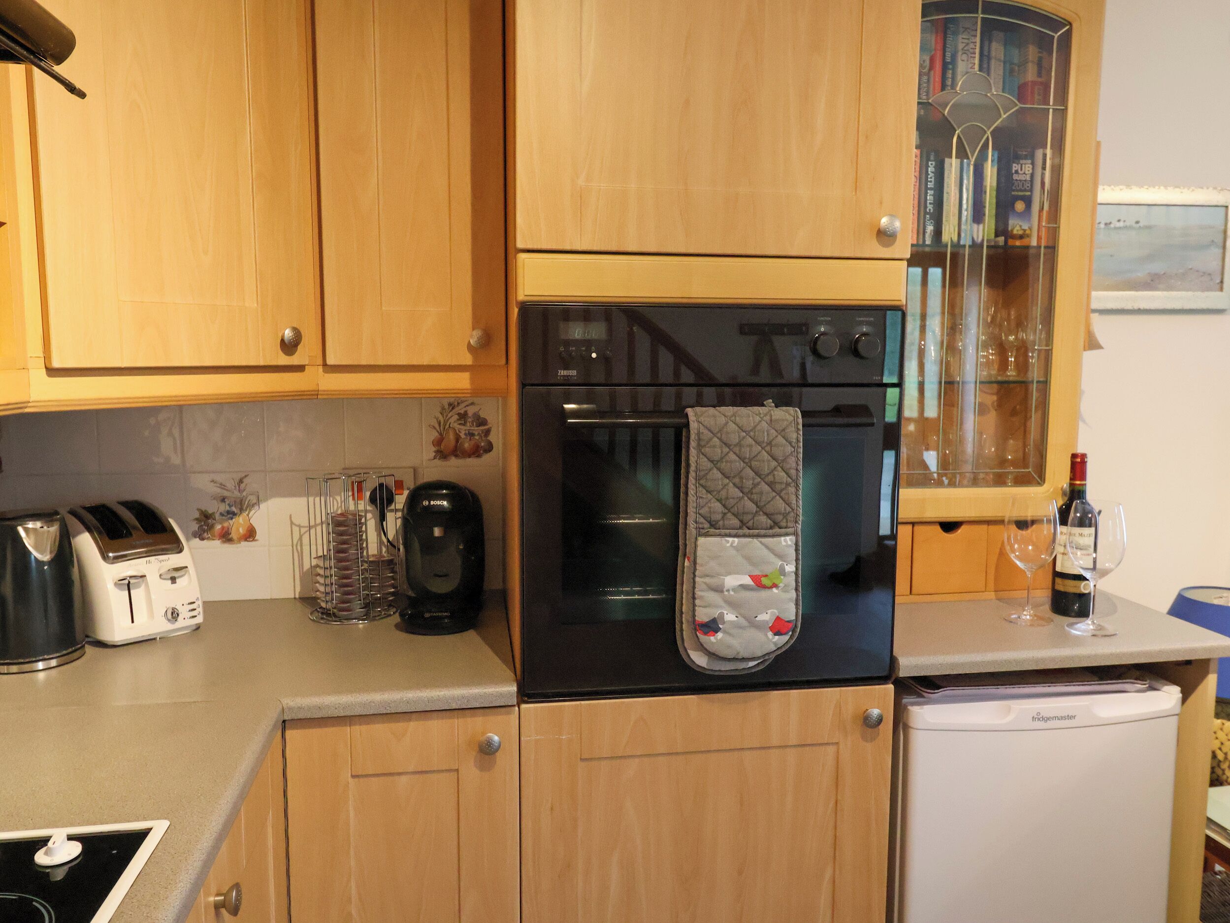 A kitchen with wooden cabinets, a Bosch coffee maker, a kettle, a toaster, and a refrigerator.