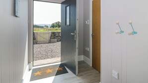 A hallway with a wooden door, a star-patterned mat, and a view of a grassy area outside. - Fasgadh (Perth)