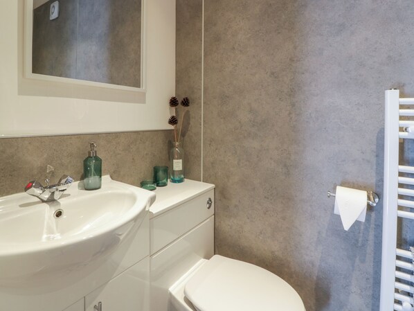 Een badkamer met een wit wastafel, spiegel en toilet. Op het aanrecht liggen decoratieve dennenappels en een groene fles.