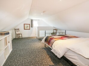 Une chambre mansardée accueillante, avec un lit, une chaise, une bibliothèque et une fenêtre.