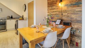 A dining area with a wooden table set for four, white chairs, a vase with flowers, and a laptop on the table. - Fasgadh (Perth)