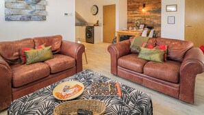 A living room with two brown leather sofas, a patterned ottoman, and a dining area with a wooden table and chairs. - Fasgadh (Perth)
