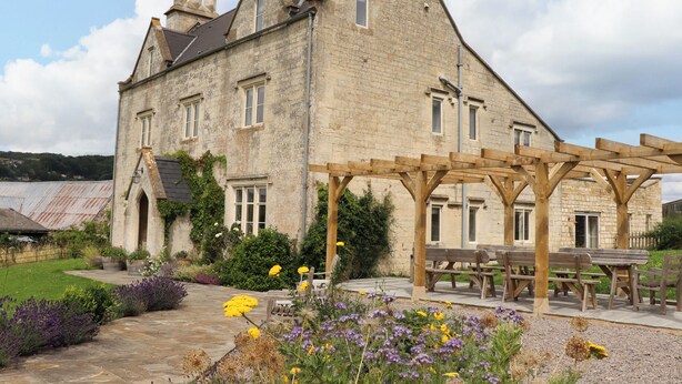 A stone building with a wooden pergola and outdoor seating area. - Hammonds Farmhouse (Stroud)