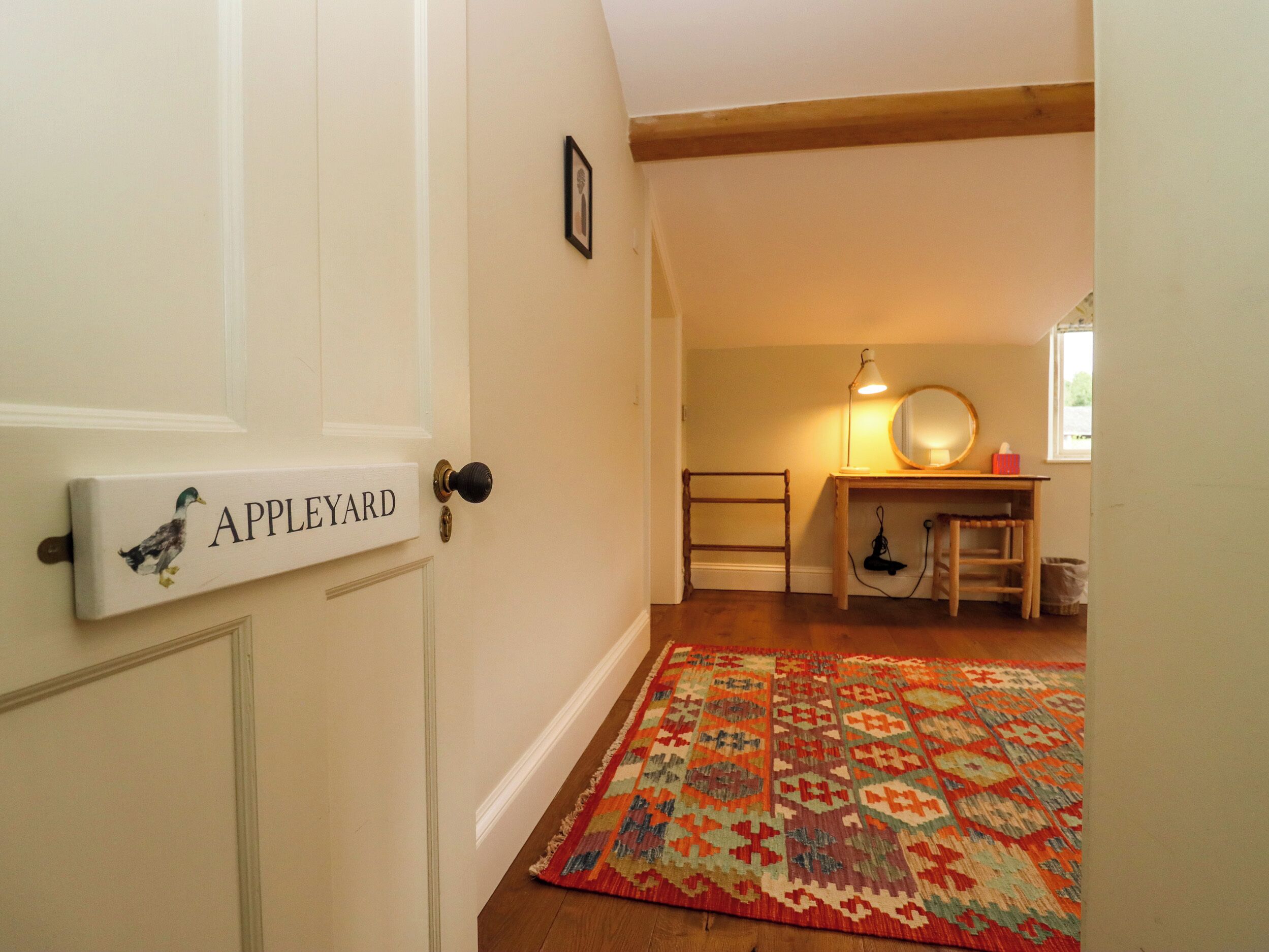 En hall med trägolv, en färgglad matta, ett skrivbord med en lampa och en dörr med texten ”APPLEYARD”.