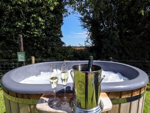 Un jacuzzi con dos copas de champán y una botella, sobre una terraza de madera con un cartel al fondo.
