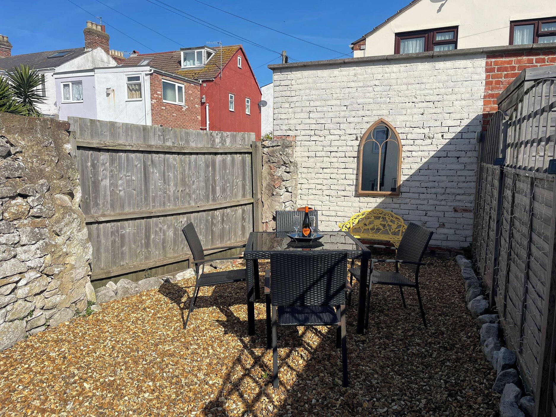 A patio with a table and chairs, a stone wall, and a wooden fence.