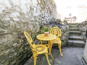 Un mur de pierre avec une petite table et deux chaises, une plante en pot et un escalier.