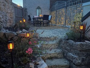 An outdoor patio area with stone steps, a table, chairs, and string lights. - Winkle Cottage (Weymouth)