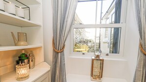 A bathroom with a window, a shelf with toiletries, and a decorative lantern. - Winkle Cottage (Weymouth)