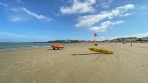 A beach with lifeguard equipment, including a red flag and a yellow surfboard. - Winkle Cottage (Weymouth)