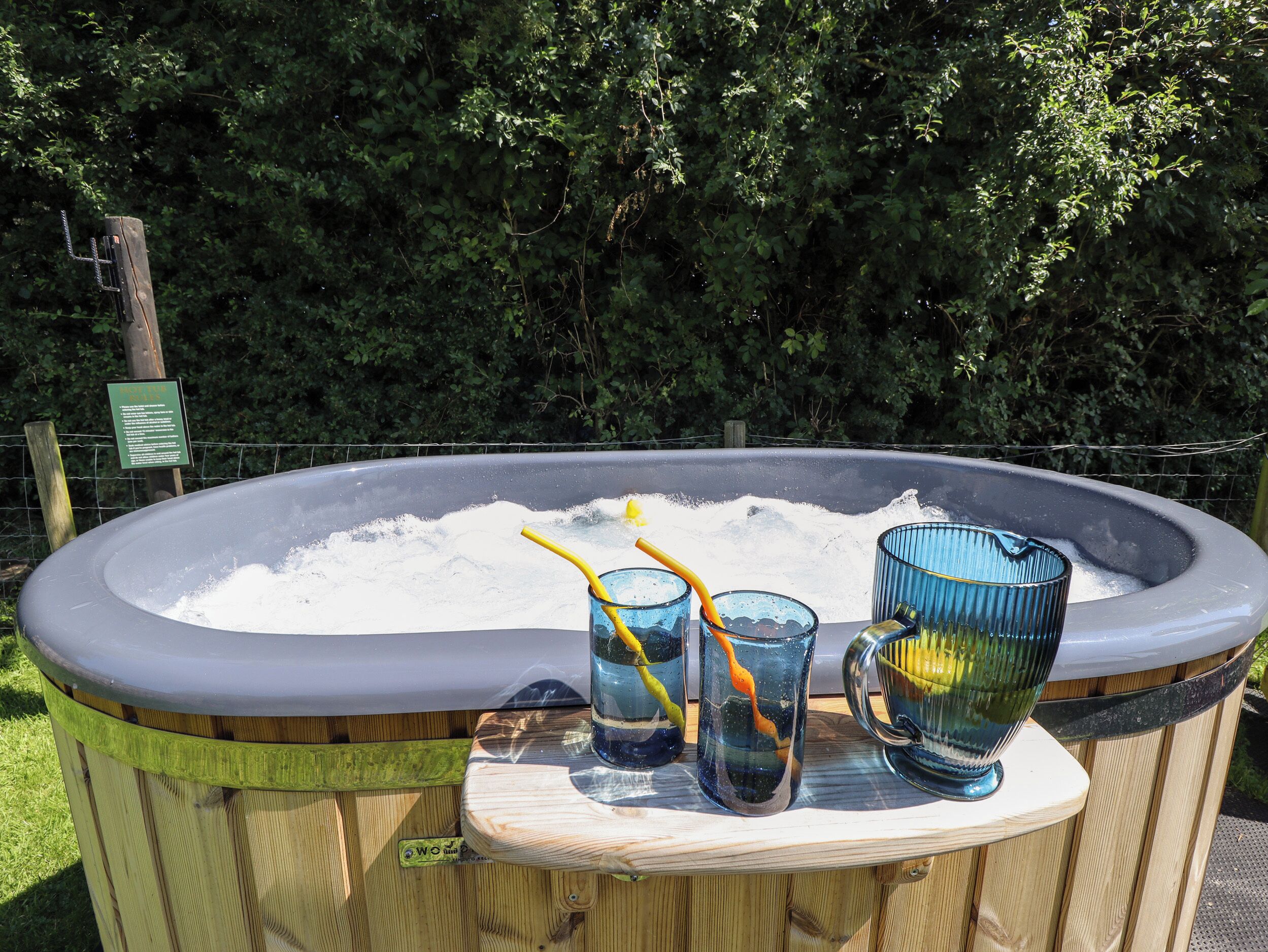 A hot tub with two glasses and a mug on a wooden platform.