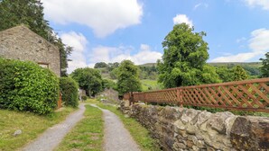 Ein Feldweg, der zu einem Steinhaus mit Holzzaun führt.