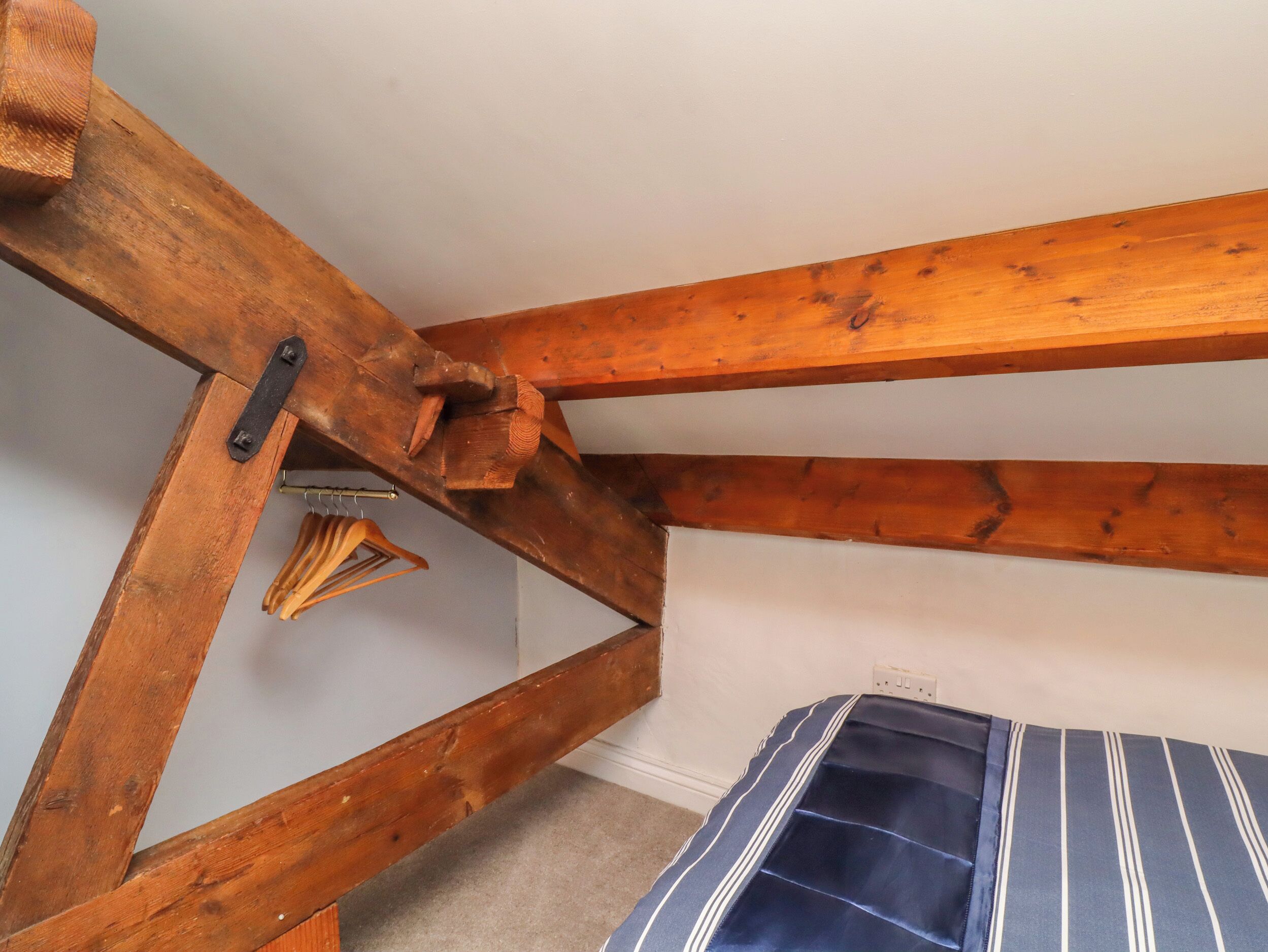 A room with exposed wooden beams, a striped mattress, and a hanging wooden hanger.