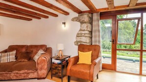 Ein gemütliches Wohnzimmer mit einem braunen Ledersofa, einem passenden Sessel, einem kleinen Holztisch mit einer Lampe und einer Steinwand.