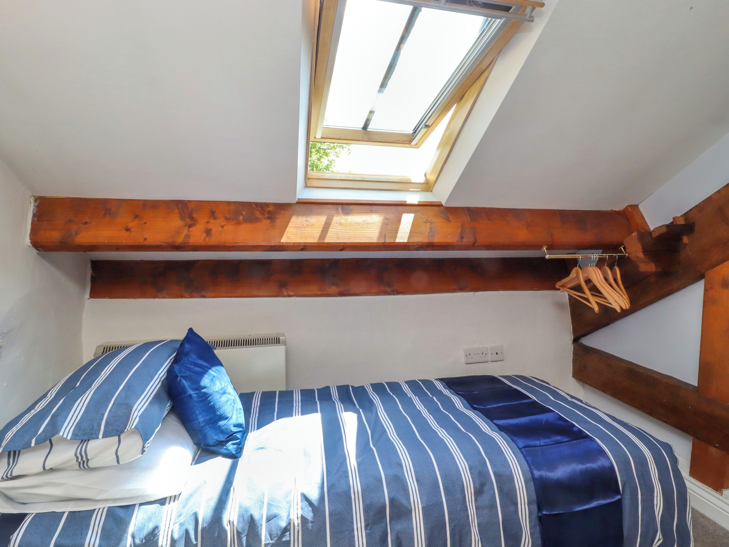 Une petite pièce accueillante, avec un plafond en pente, un puits de lumière, un lit avec une literie à rayures et un banc en bois.