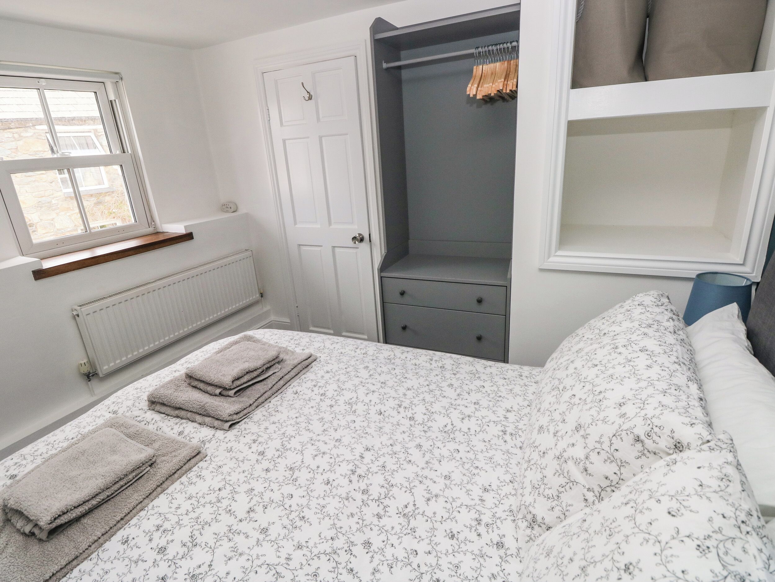 Un dormitorio con cama, armario, radiador y ventana.