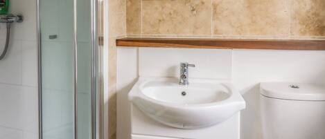 A bathroom with a glass shower enclosure, a white sink with a chrome faucet, and a toilet.