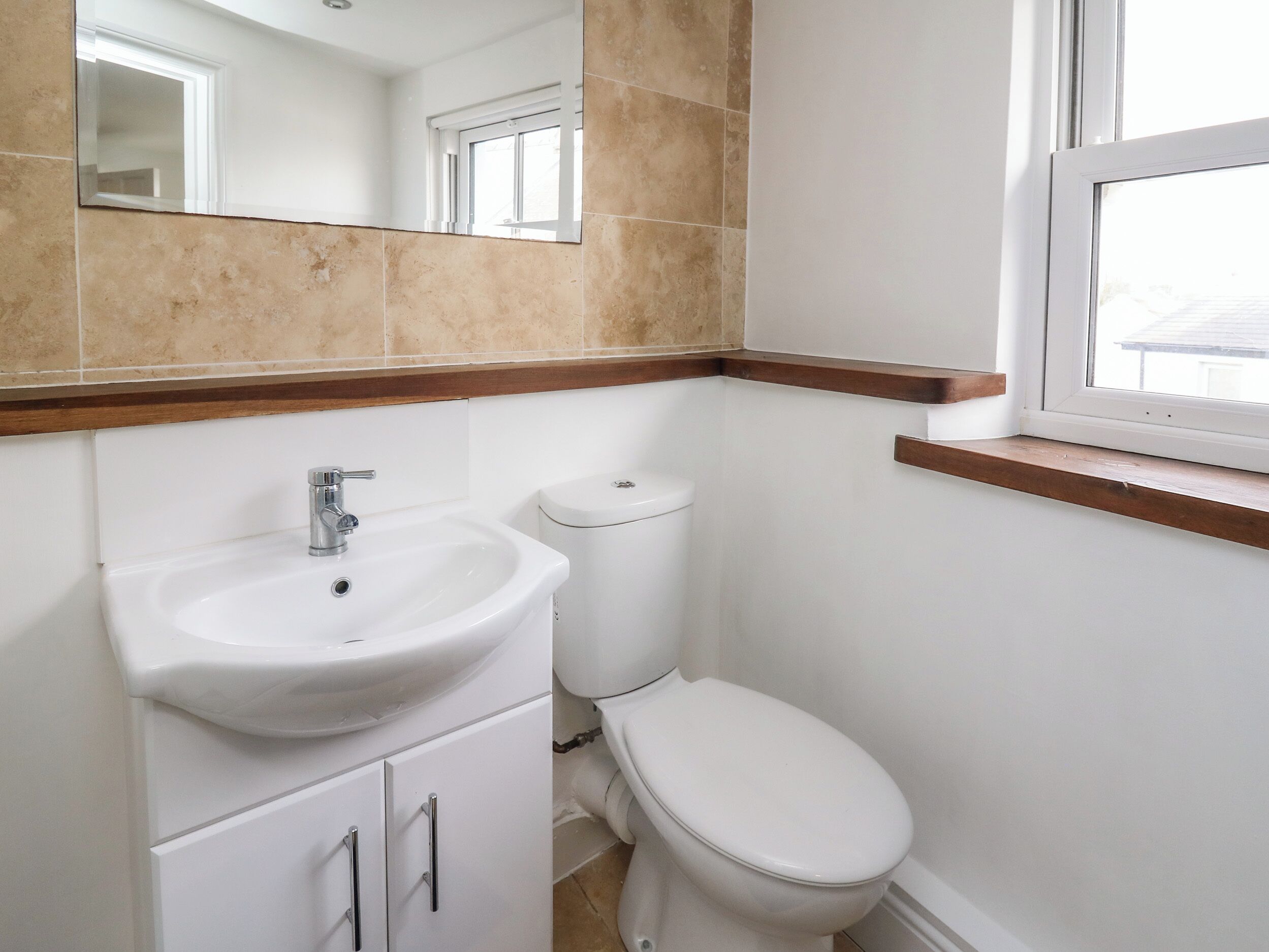 A bathroom with a white sink, toilet, and a window above the toilet.