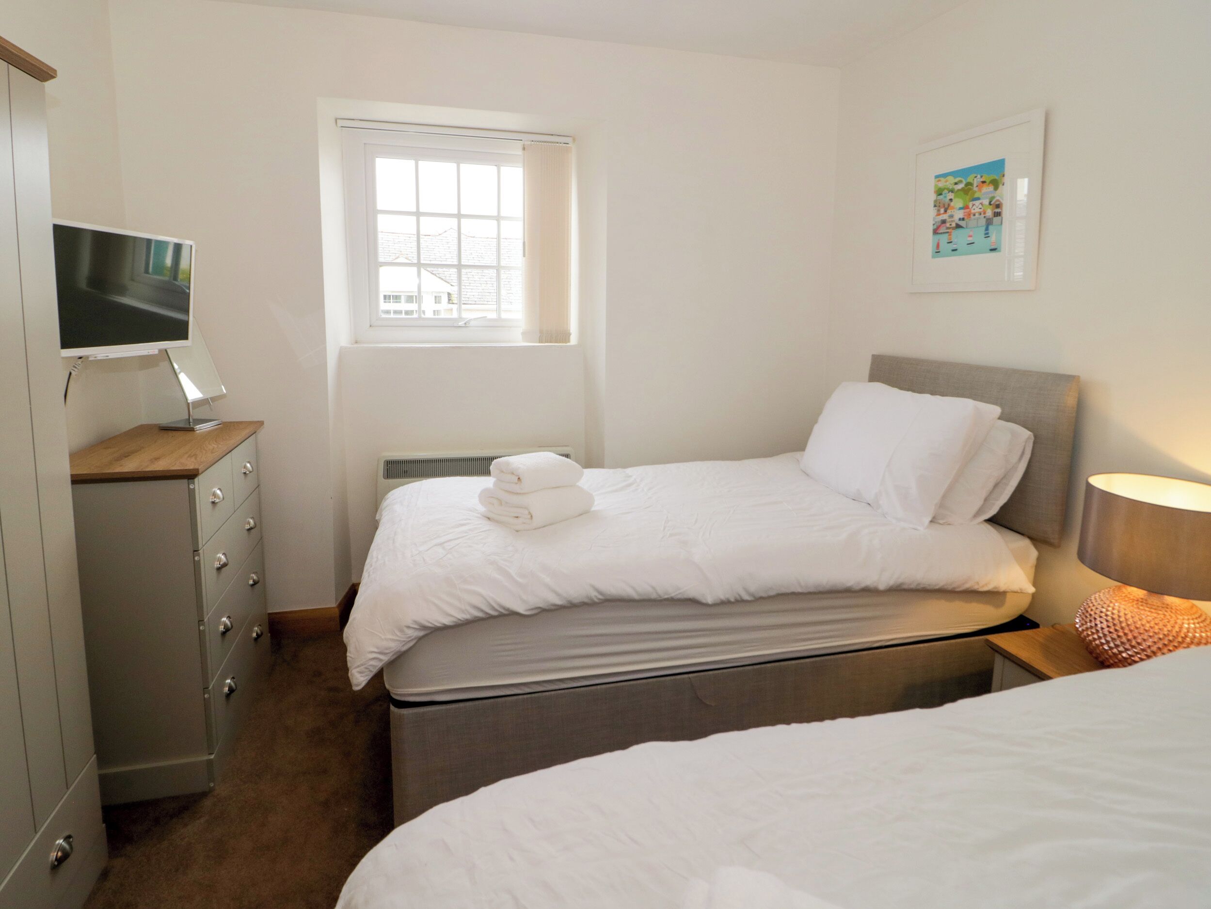 Un dormitorio con una cama, un escritorio con computadora, una ventana y un cuadro en la pared.