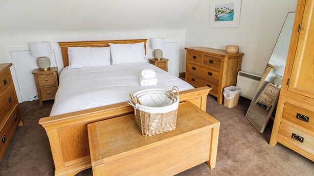 Une chambre à coucher bien rangée, avec un grand lit, des tables de chevet en bois, une table de chevet avec un panier et une commode.