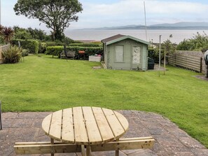 A wooden picnic table with benches in a grassy yard with a view of the sea. - 3 Moranedd (Moelfre)