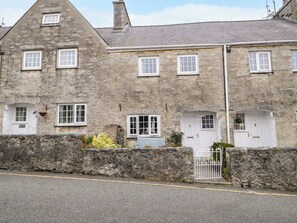 A stone building with multiple windows and doors, a stone wall in front, and a gated entrance. - 3 Moranedd (Moelfre)