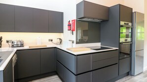 A modern kitchen with dark cabinetry, a built-in oven, and a stainless steel refrigerator. - The Hayloft (Appleby-in-Westmorland)