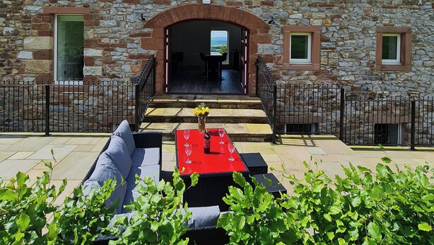 A stone building with a red table and outdoor seating. - The Hayloft (Appleby-in-Westmorland)