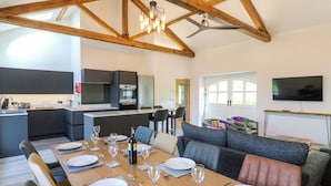 A modern kitchen with dark cabinets, a dining area with a wooden table set for six, and a large window with a view of greenery. - The Hayloft (Appleby-in-Westmorland)