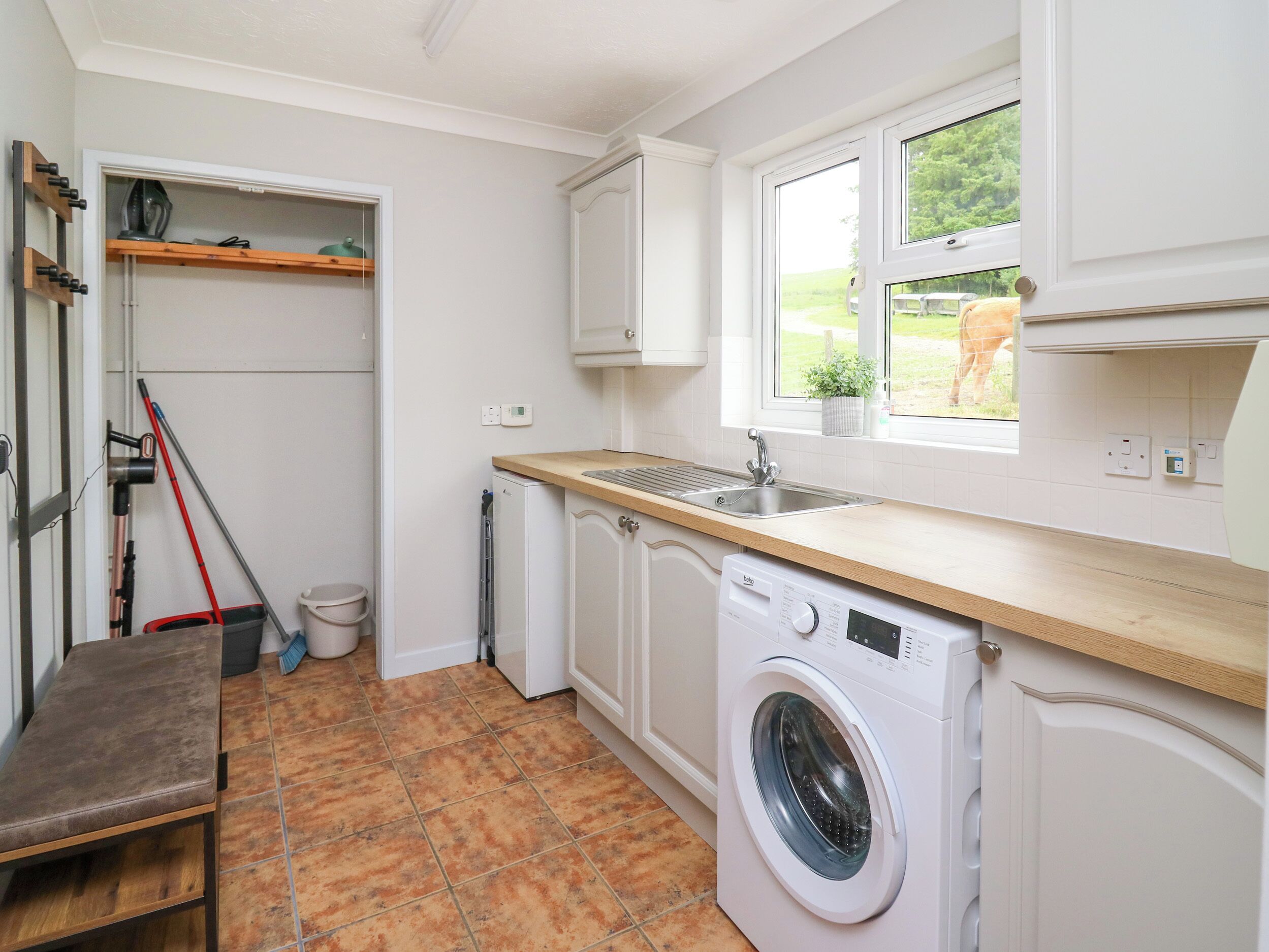 Cocina compacta con lavadora, lavaplatos y ventana que da a vista de un caballo.
