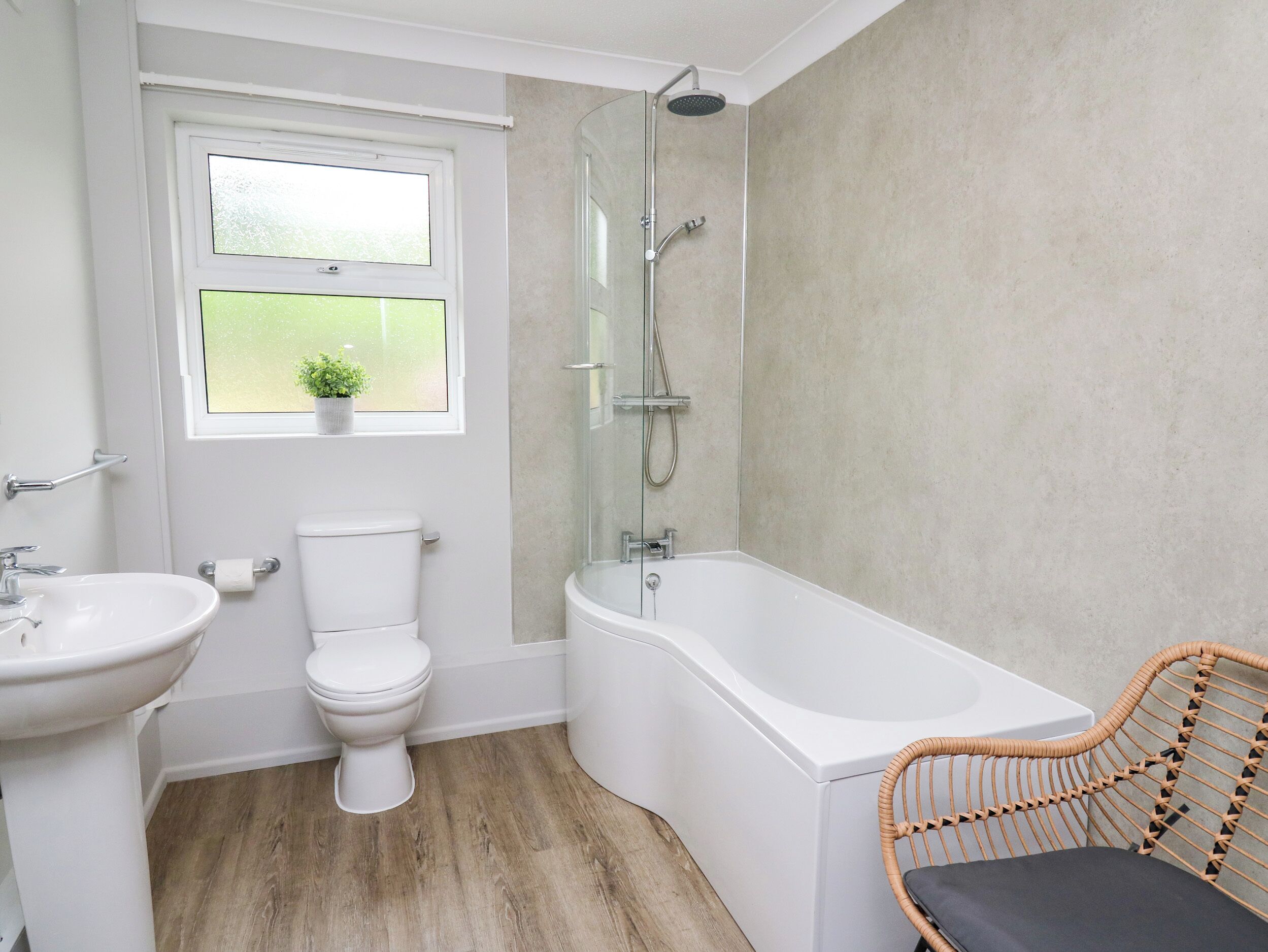 A bathroom with a toilet, sink, shower, and a wicker chair.