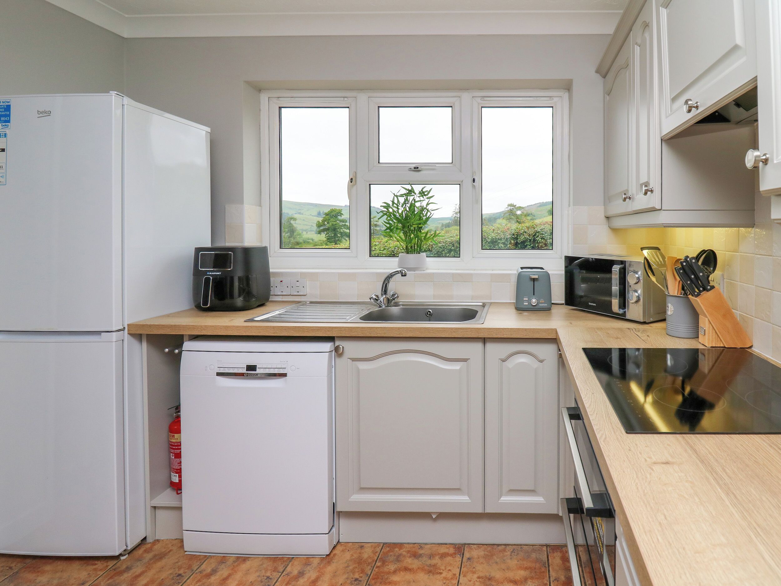 A modern kitchen with white cabinets, a built-in dishwasher, a coffee maker, a toaster, and a window with a view of greenery.